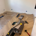 Room under renovation with wooden flooring, tools, and materials.